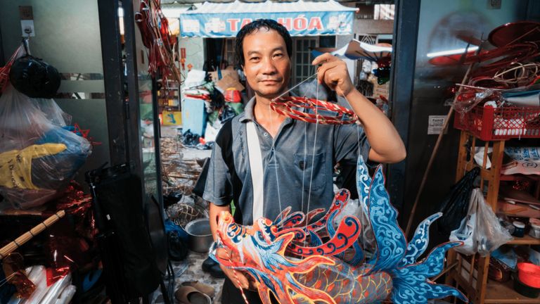 Nguyen Trong Binh, a third-generation artisan from Bao Dap village, with a fish-shaped lantern—one of his recent creations. | Photo by Danky for Vietcetera.